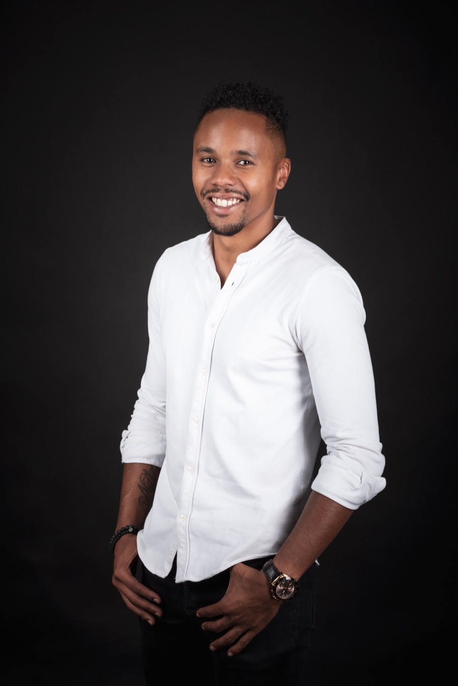 Portrait de Steven Giron, souriant, en chemise blanche sur fond noir